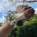 A white rose, baby’s breath and green leaves arranged as a wrist corsage.